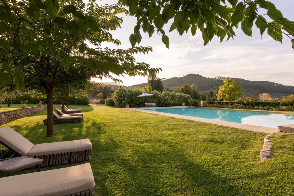 Villa Elisa poolside garden at dusk with sun loungers and rolling hills, Lucca, Italy