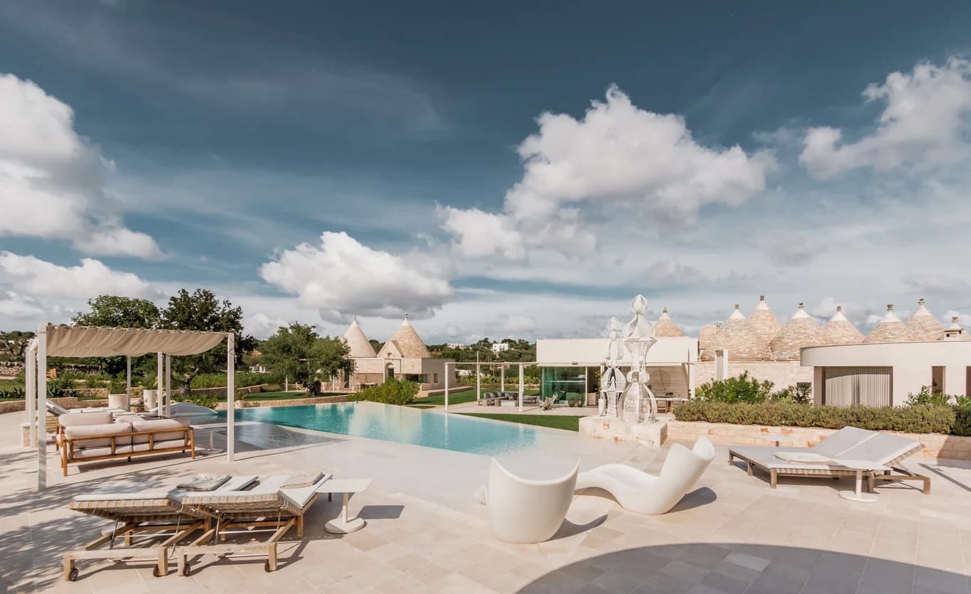 Dimora Dieci Coni pool deck with travertine terrace and trulli backdrop, Cisternino, Italy