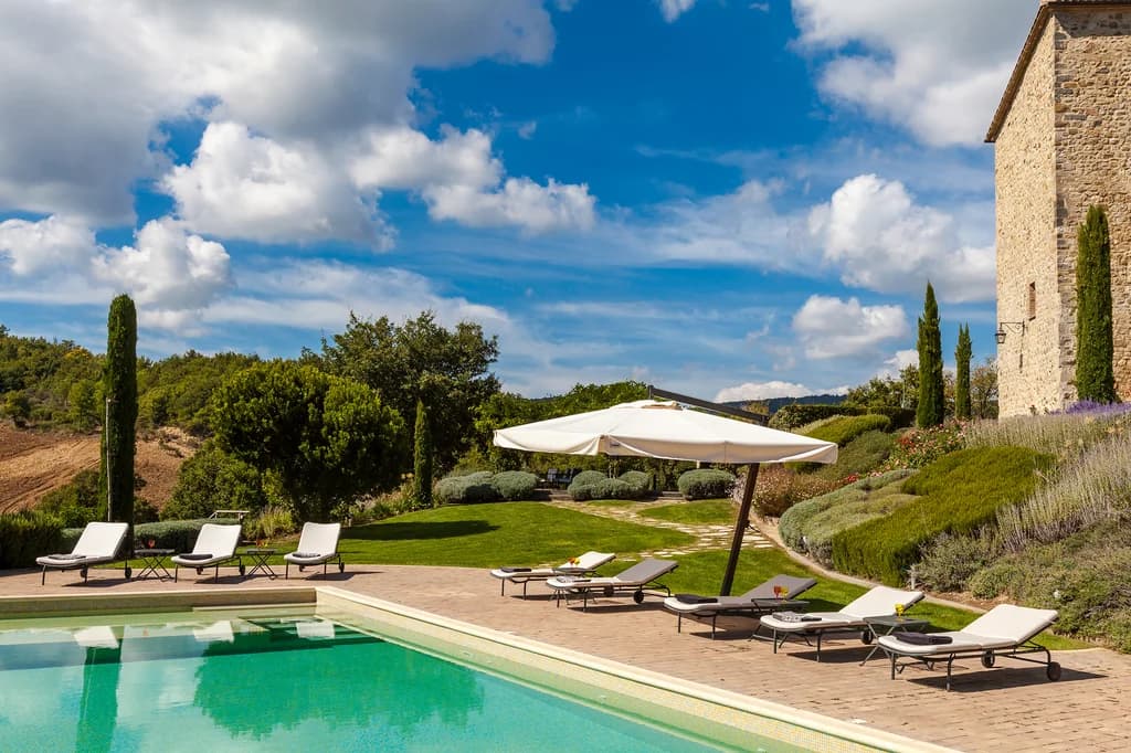 Villa Chianina outdoor pool terrace with sun loungers, cypress trees and stone walls, Fabro, Italy